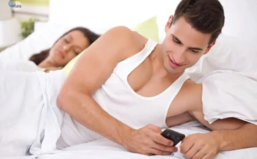 Pareja en cama, hombre revisando celular