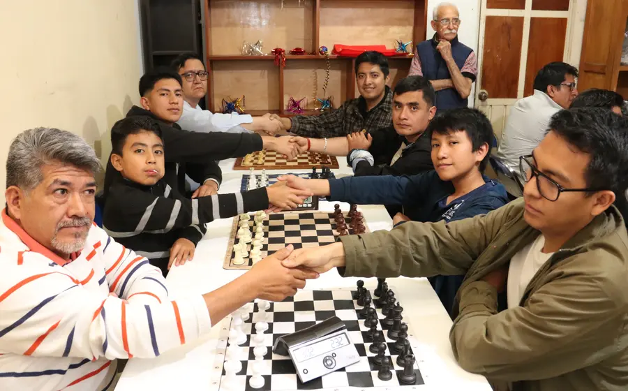Dos jugadores de ajedrez se dan la mano sobre el tablero en un saludo tradicional antes de comenzar su partida en el Torneo Rábanos.
