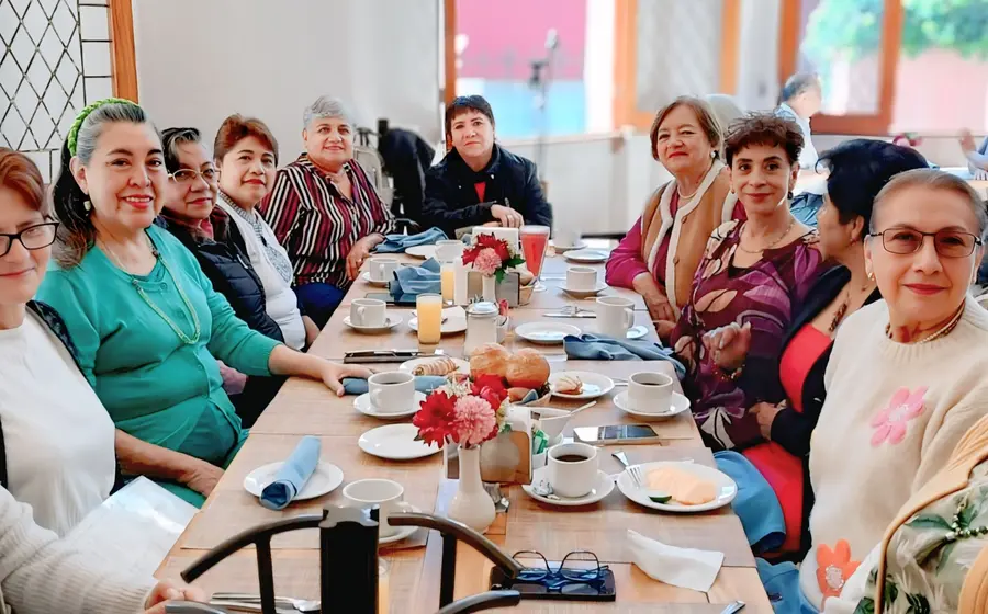 Lilí Mayoral, con blusa morada, sonríe rodeada de sus amigas durante la celebración de su cumpleaños, compartiendo un momento feliz entre ellas.