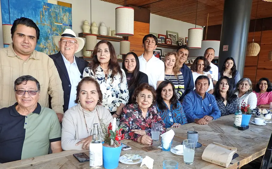 La señora Sofía Morales Zárate, sentada y usando una blusa de flores, celebra su cumpleaños rodeada por su amorosa familia.