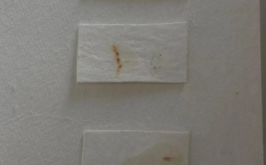 Primer plano de una prueba de ventana que muestra el resultado de un test de solubilidad con agua sobre un antiguo documento histórico.