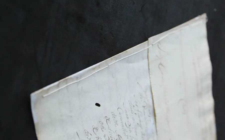 Primer plano de la reposición de costura en un documento colonial del siglo XVII, mostrando una técnica de intervención para su preservación.