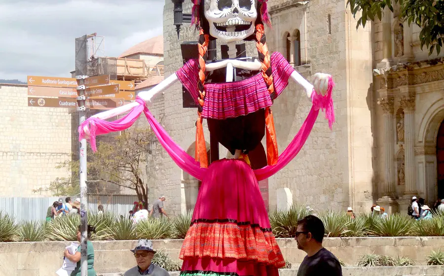 Un grupo de turistas posa sonriente junto a las calaveras gigantes que adornan el Andador Turístico de Oaxaca durante las festividades de Día de Muertos.