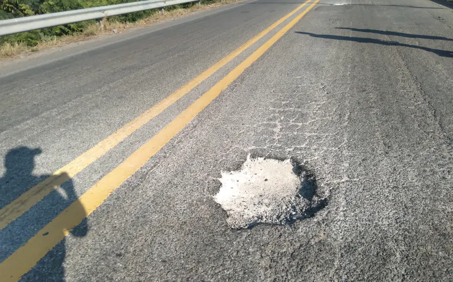 Un primer plano de un enorme bache en una carretera de Tehuantepec, ilustrando el peligro que causa pinchaduras de neumáticos a los vehículos.