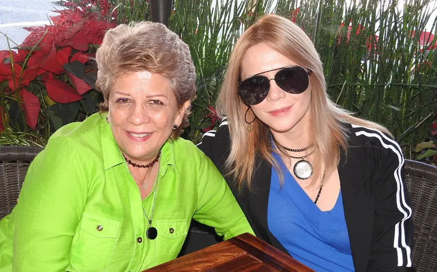 Adriana Hurtado y Marcela Mendiola posan juntas y sonrientes para la cámara durante un evento social, compartiendo un momento feliz.