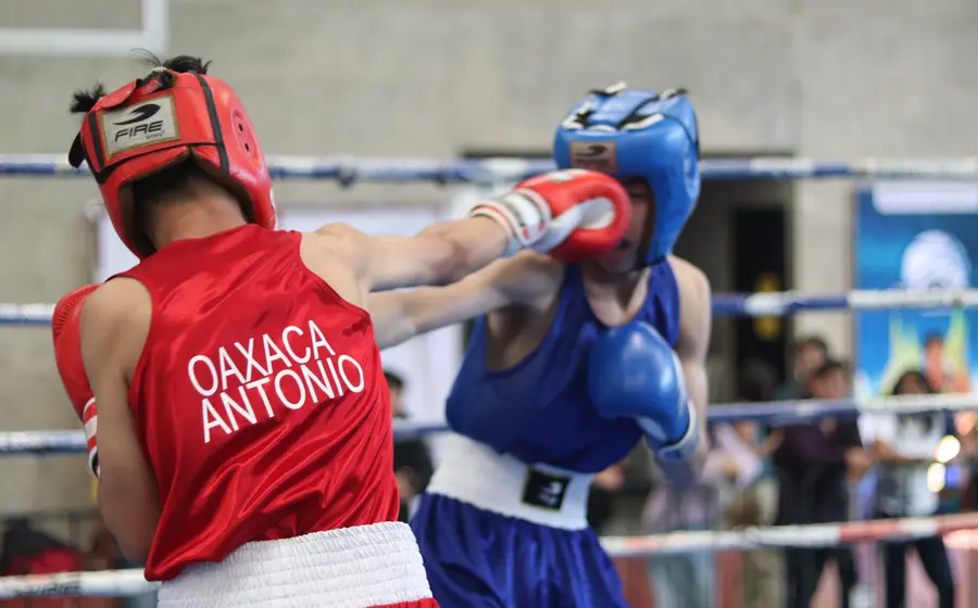 Dos jóvenes boxeadores intercambian puñetazos con fuerza durante un combate reñido correspondiente a la Olimpiada Estatal de Boxeo.