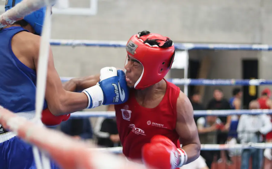 Dos jóvenes pugilistas intercambian golpes durante un duro combate de boxeo en la Olimpiada Estatal celebrada en el Gimnasio Ricardo Flores Magón.