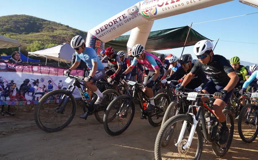 Un grupo de ciclistas de montaña arrancan con fuerza y determinación en la línea de salida de una competencia en la sierra.