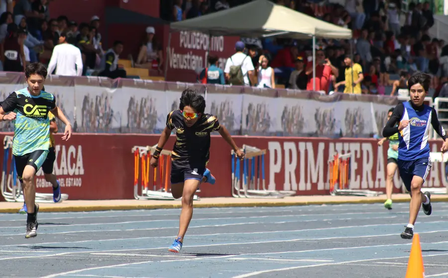 Un atleta cruza la línea de meta con gran esfuerzo y determinación durante una competencia de la Olimpiada Estatal de Atletismo.