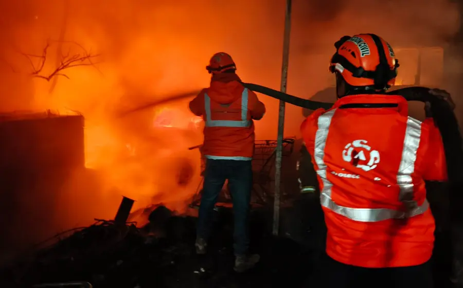 Tres vehículos completamente calcinados se observan dentro de un taller de hojalatería, mostrando los daños ocasionados por un fuerte incendio en el lugar.