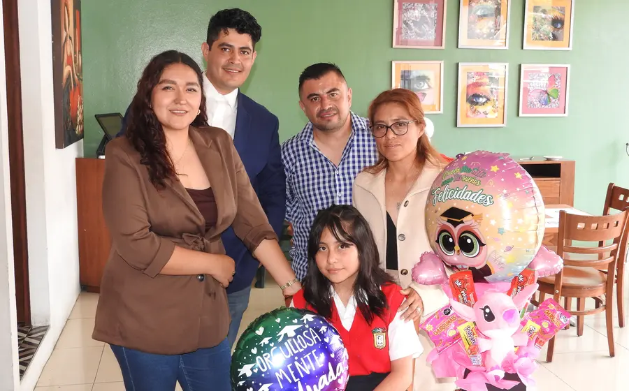 Frida Madai celebra la culminación de sus estudios primarios, posando felizmente junto a sus padres y padrinos durante el festejo del acontecimiento.