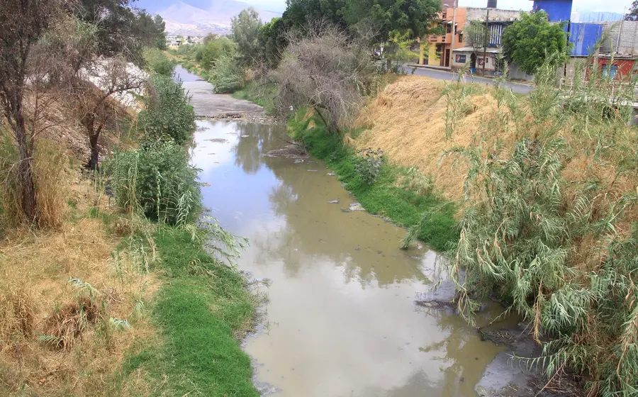 Una imagen que muestra varias casas y edificios construidos peligrosamente sobre el bordo de un río, invadiendo el cauce natural del agua.