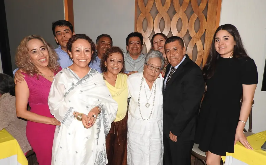 La señora Doris Calvo Cruz, vistiendo un elegante traje blanco, celebra su cumpleaños sonriendo rodeada del cariño de sus familiares y amistades.