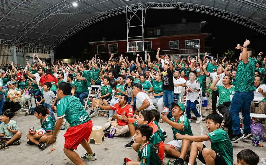 Familias y aficionados abarrotan una plaza pública en Juchitán para ver un partido del Mundial, creando un ambiente de fiesta y celebración comunitaria.