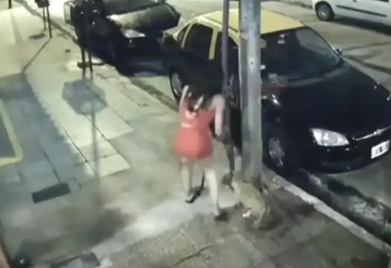 Una mujer acompañada de un niño apresuradamente ata al cachorro en un poste de la calle. 