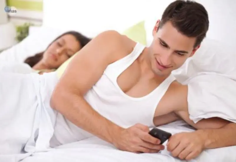 Pareja en cama, hombre revisando celular