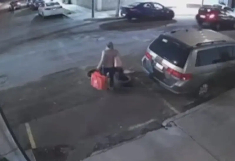 La mujer no se percata que delante de ella hay una coladera sin tapa.