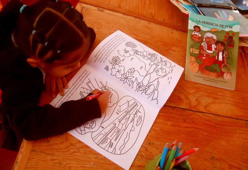 Una alumna de segundo grado de preescolar colorea el cuento La Herencia de Tita que honra el trabajo de alimentación sana de las cocineras tradicionales.