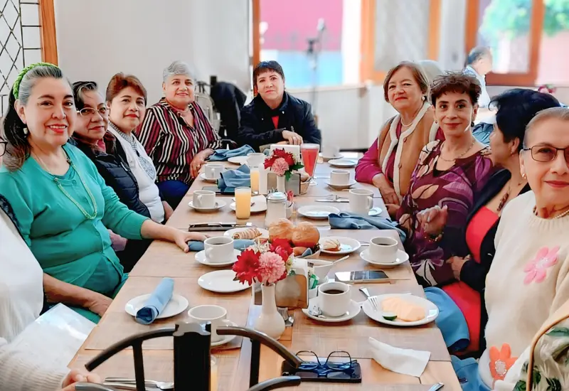 Lilí Mayoral, con blusa morada, sonríe rodeada de sus amigas durante la celebración de su cumpleaños, compartiendo un momento feliz entre ellas.