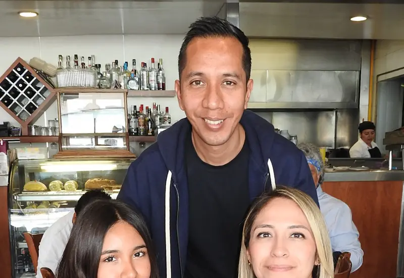 Renata Ceballos, Olga Vásquez y Óscar Ceballos sonríen juntos mientras disfrutan de un agradable momento con un café en un evento social.