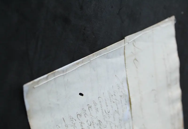 Primer plano de la reposición de costura en un documento colonial del siglo XVII, mostrando una técnica de intervención para su preservación.