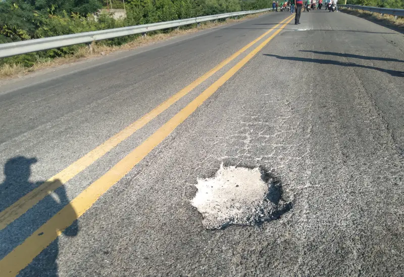 Un primer plano de un enorme bache en una carretera de Tehuantepec, ilustrando el peligro que causa pinchaduras de neumáticos a los vehículos.