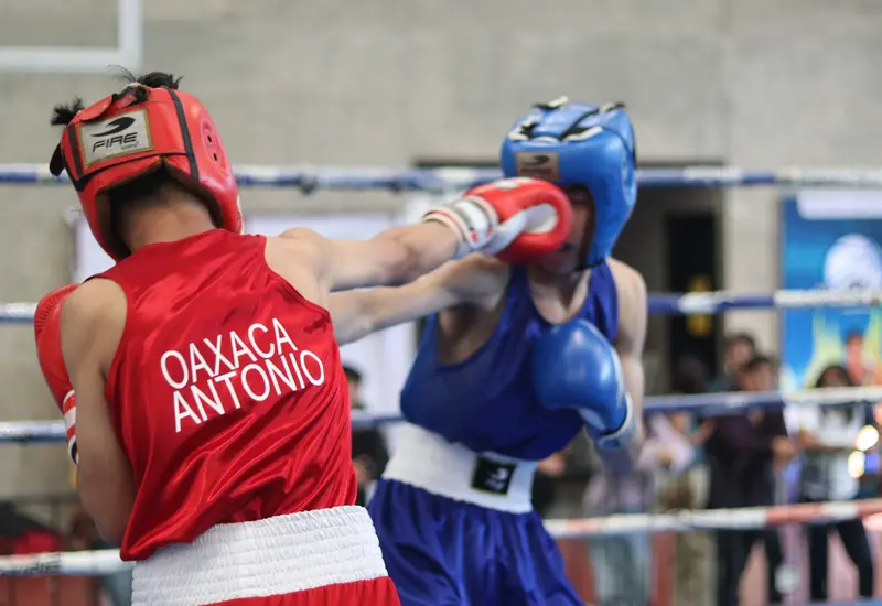 Dos jóvenes boxeadores intercambian puñetazos con fuerza durante un combate reñido correspondiente a la Olimpiada Estatal de Boxeo.