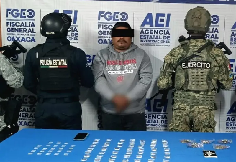 Un hombre detenido por narcomenudeo es presentado por las autoridades junto a los paquetes de droga que le fueron asegurados durante su captura.