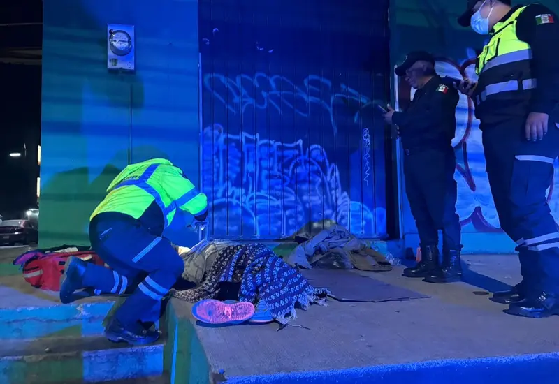 Una mujer en situación de calle yace sin vida sobre la banqueta en la vía pública, evidenciando una lamentable situación de abandono.
