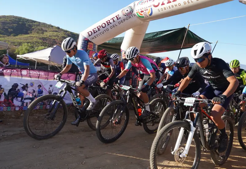 Un grupo de ciclistas de montaña arrancan con fuerza y determinación en la línea de salida de una competencia en la sierra.