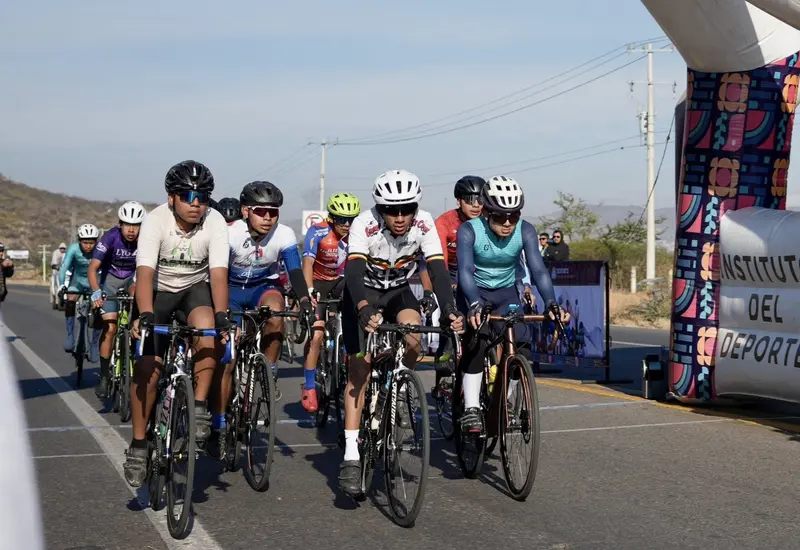 Un grupo de ciclistas avanza en formación durante una competencia de ciclismo de ruta, componiendo uno de los bloques de competidores.