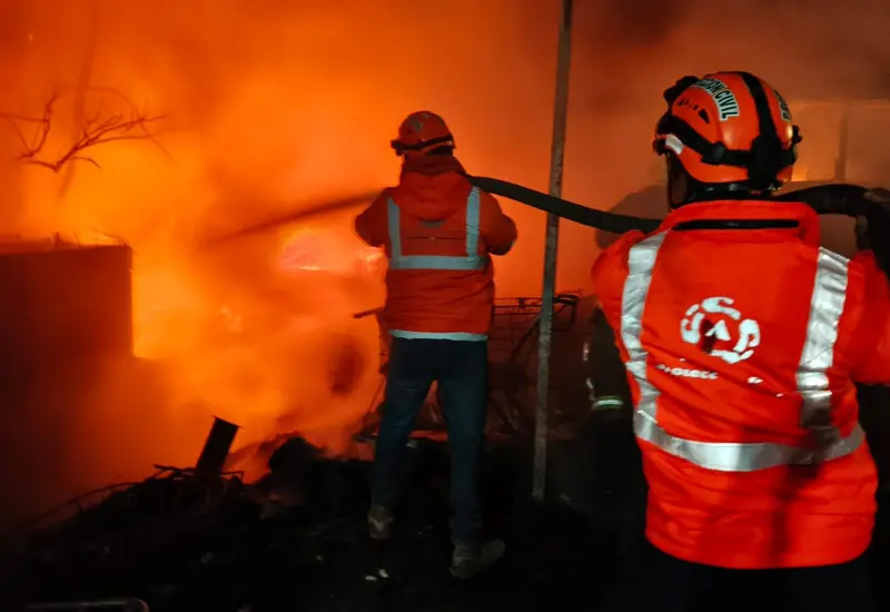 Tres vehículos completamente calcinados se observan dentro de un taller de hojalatería, mostrando los daños ocasionados por un fuerte incendio en el lugar.