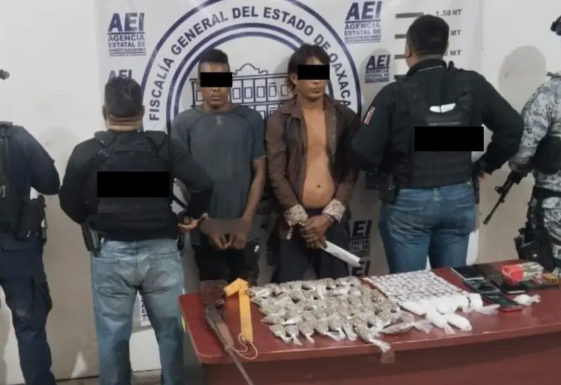 Dos personas detenidas son presentadas junto a una mesa con las dosis de droga y las armas aseguradas durante el operativo de seguridad.