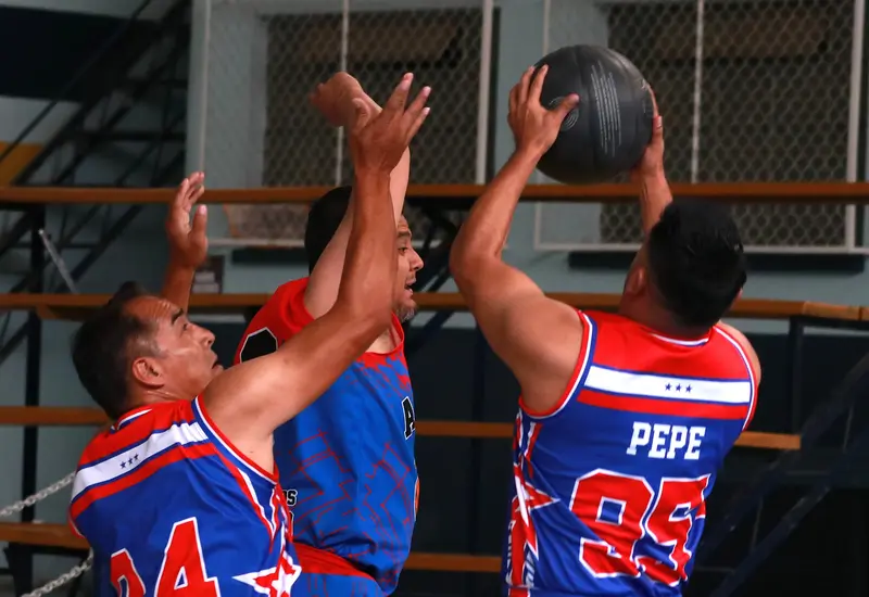 Jugadores del equipo campeón de la liga de baloncesto de veteranos luchan por obtener el rebote durante un partido de la final.