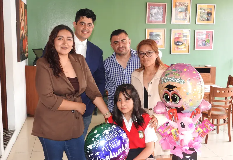 Frida Madai celebra la culminación de sus estudios primarios, posando felizmente junto a sus padres y padrinos durante el festejo del acontecimiento.