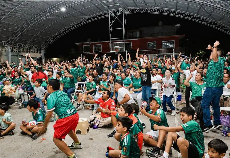 Familias y aficionados abarrotan una plaza pública en Juchitán para ver un partido del Mundial, creando un ambiente de fiesta y celebración comunitaria.