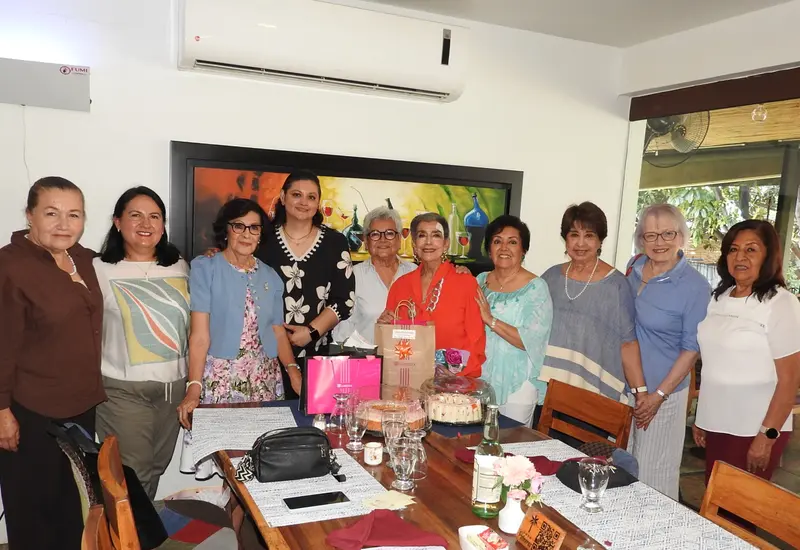 La maestra Lupita Aquino posa sonriente en el centro durante la emotiva celebración de su cumpleaños, rodeada por su grupo de amigas.