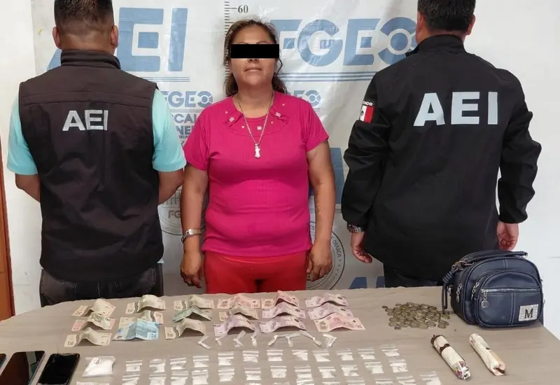 Una mujer detenida es presentada por las autoridades junto a una mesa donde se exhibe la presunta droga y el dinero asegurado durante el operativo.